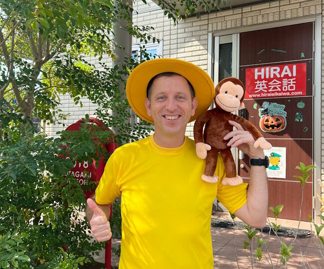 ハロウィンパーティーが近づいている。教室の入り口で黄色のTシャツと帽子を身につけた主任教師が立っており、左肩には好奇心旺盛なジョージがいる。